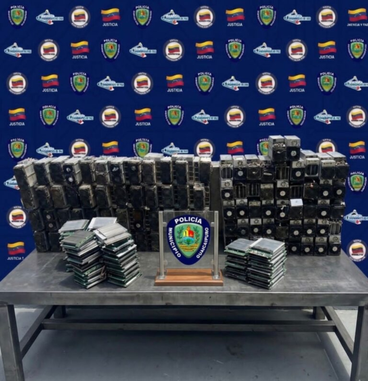 Funcionarios del Servicio de Investigación Penal (SIP) del Instituto Autónomo de Policía Municipal de Guaicaipuro, en conjunto con funcionarios de la Guardia Nacional Bolivariana (GNB), ejecutaron el desmantelamiento de un importante lote de minería digital que operaba en la parroquia Los Teques, estado Miranda. El procedimiento tuvo lugar en una vivienda de la urbanización Piedra Azul, comunidad de Lagunetica. Durante la inspección, los efectivos policiales detectaron una infraestructura tecnológica no declarada, presuntamente utilizada para el procesamiento de algoritmos criptográficos en perjuicio del sistema eléctrico nacional del Estado venezolano. En el sitio, los funcionarios incautaron un importante lote de equipos, entre los que destacan: 70 minadores de alta potencia (modelos Whatsminer M30S y Antminer), la mayoría operativos y con fuentes de alimentación integradas. 61 tarjetas de circuito impreso (PCB) con microprocesadores especializados para cálculos de hashing, además de 17 fuentes de poder conmutadas de alto rendimiento. 3 computadoras de escritorio marca ThinkCentre, una laptop Sony VAIO y diversas piezas de repuesto para el mantenimiento de la granja digital. El jefe policial resaltó que estas acciones forman parte de los planes de vigilancia estratégica para frenar actividades tecnológicas cladestinas que sobrecargan los servicios El caso fue notificado al ministerio Público del Estado Bolivariano de Miranda, el organismo que coordinará las actuaciones legales correspondientes para determinar las responsabilidades penales del caso. Con este golpe, los cuerpos de seguridad de la región reafirman su compromiso con la protección de los recursos nacionales y la legalidad tecnológica.